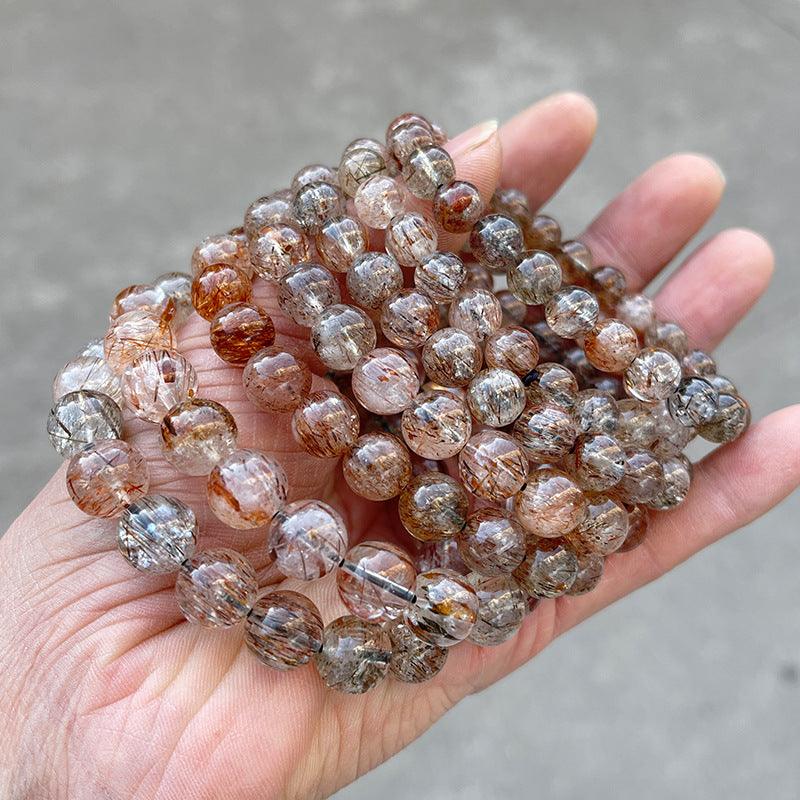 Hand holding multiple beaded black gold super 7 bracelet strands with gold brown rutile inclusions