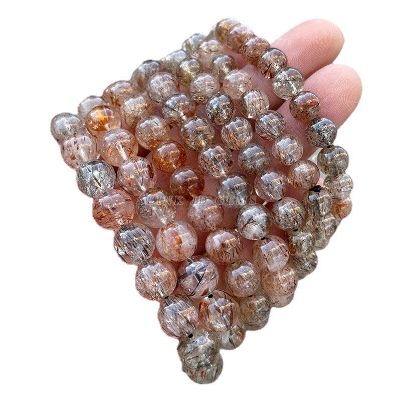 Hand holding strands of faceted round gemstone beads black gold super 7 bracelet with rutile inclusions and amber tones