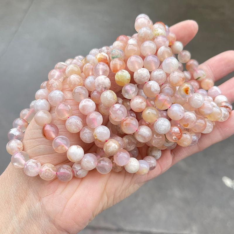 Hand holding multiple pink and peach round beaded natural stone wholesale flower agate bracelet strands
