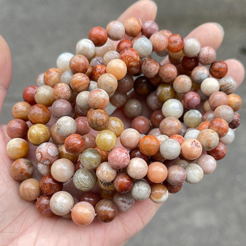 Hand holding multiple polished round beaded coral jade bracelet wholesale strands in mixed coral peach beige tones