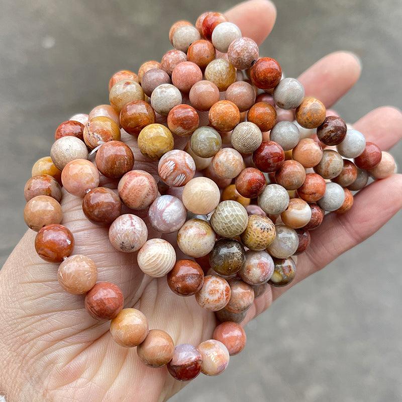 Hand holding multiple polished round coral jade bracelet wholesale strands in warm coral peach cream tones